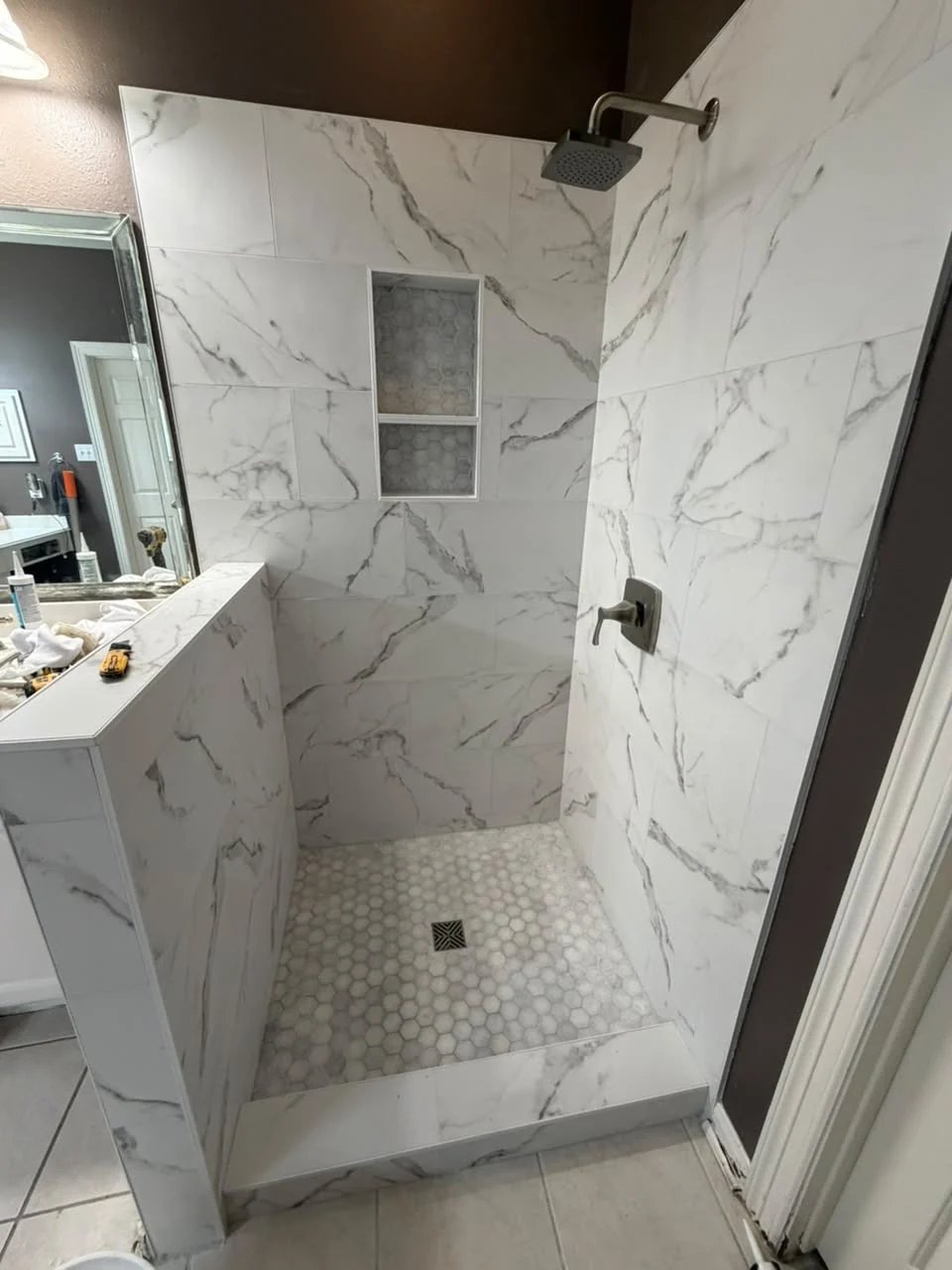 Shower with white marble-look tile, a half wall, a two-shelf niche lined in hexagon mosaic, a rain shower and a white hexagon mosaic floor.