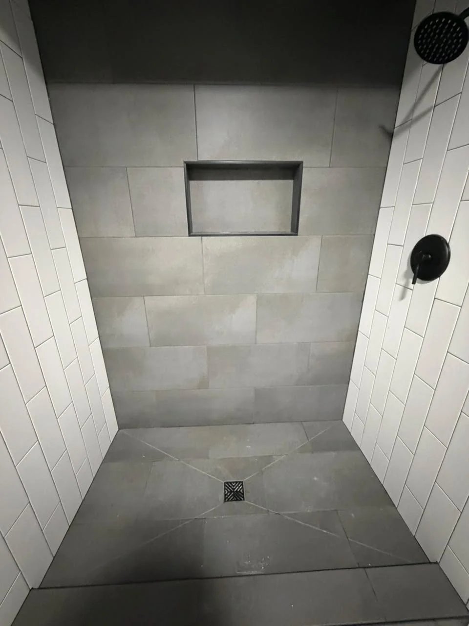 Shower with grey large-format tile on the back wall, white vertical subway tile on the sides, a recessed niche, matte black fixtures and a sloped grey tile floor.